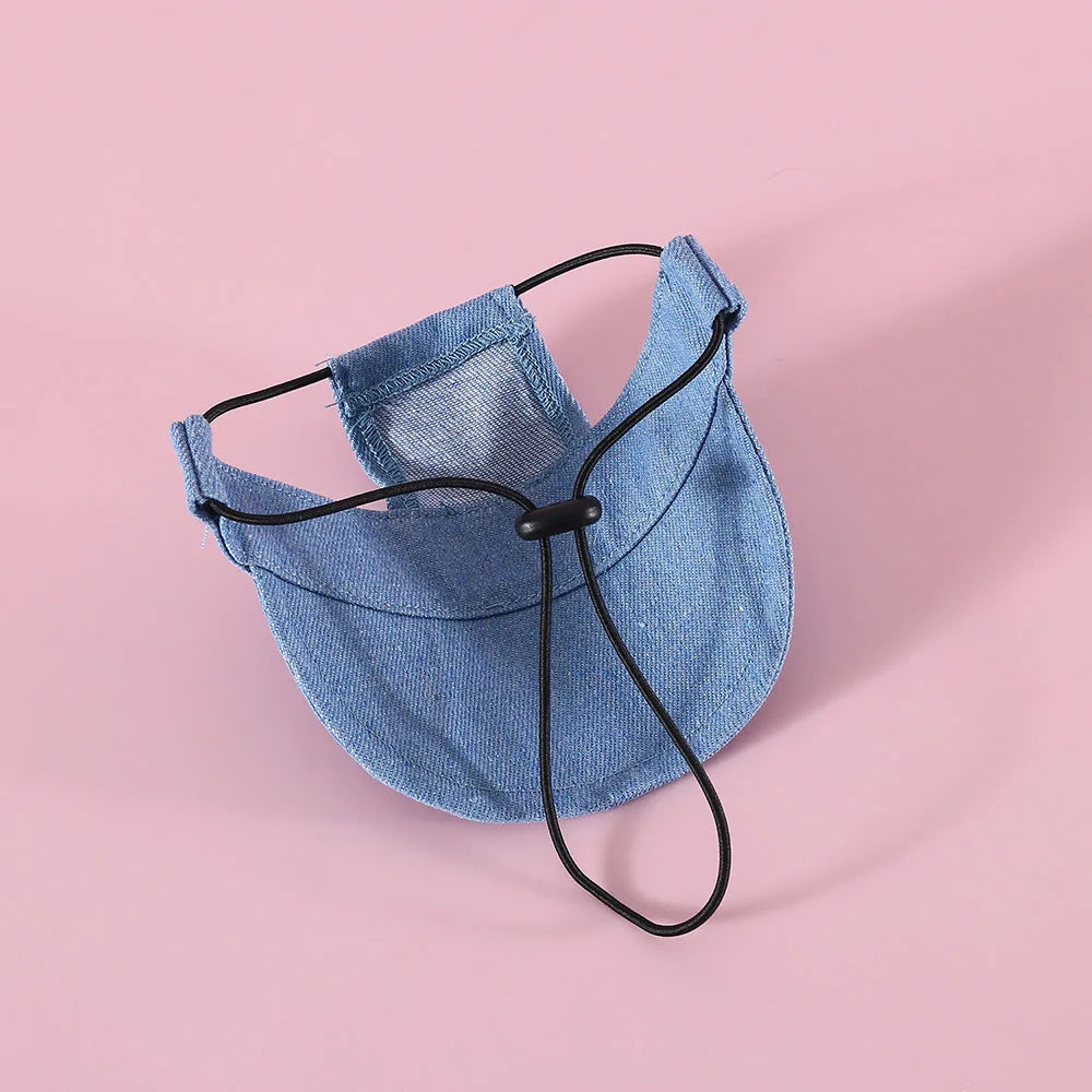 Blue denim dog hat with black strap on a pink background