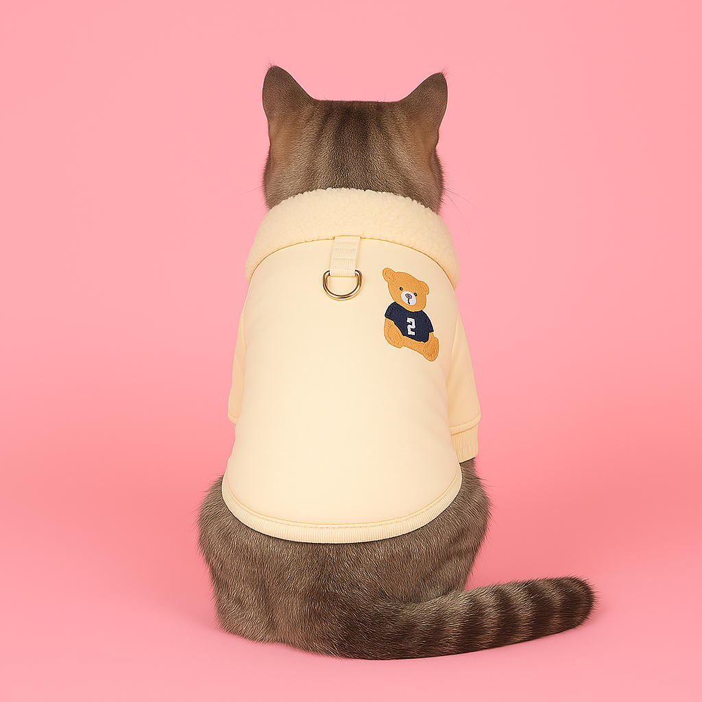 Cat wearing a beige sweatshirt with a logo on a pink background