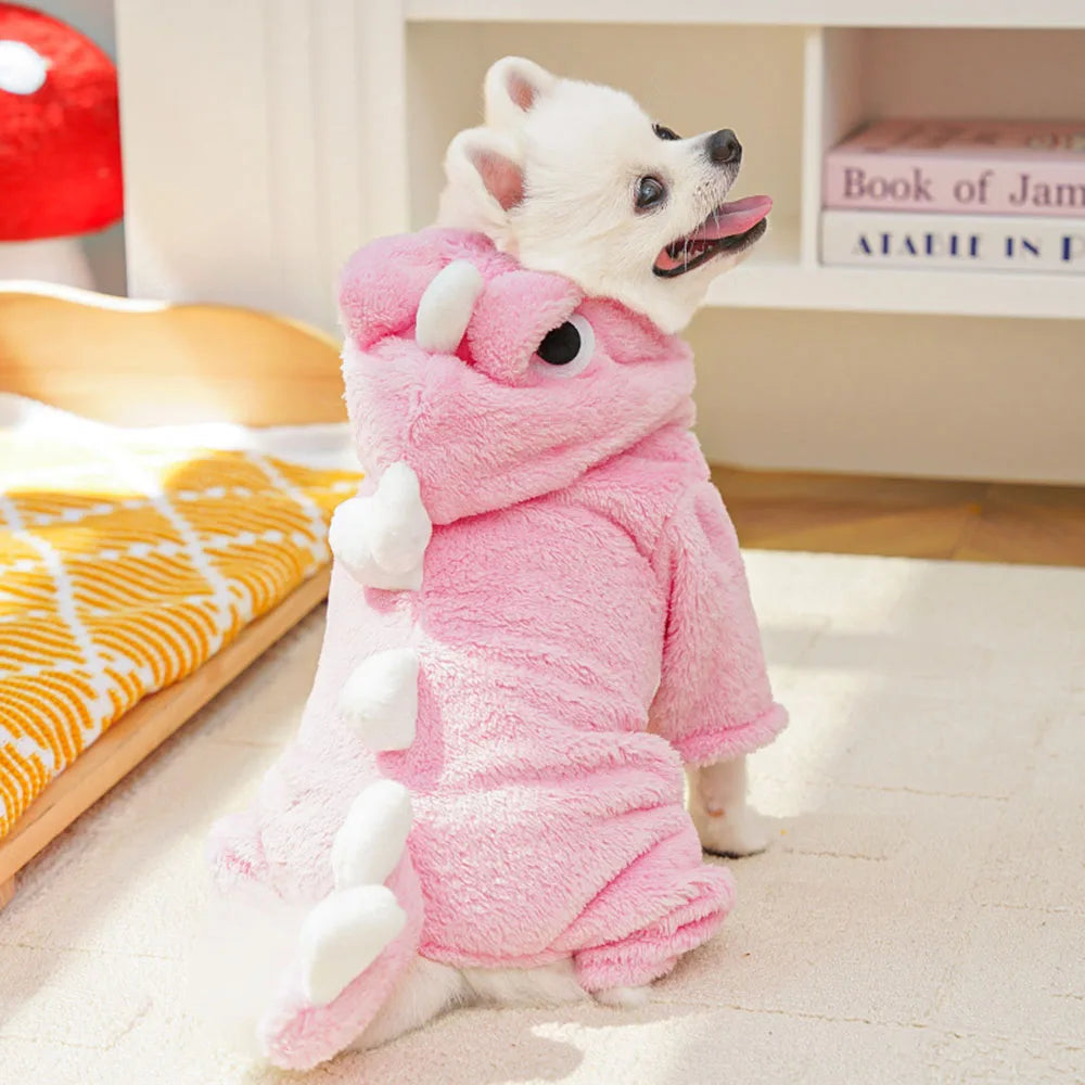 Dog wearing a pink dinosaur costume on a light-colored floor.