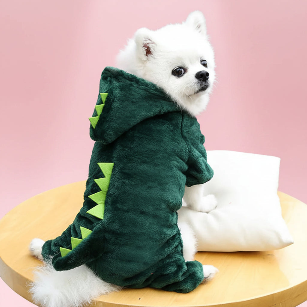 White dog wearing a green dinosaur costume on a wooden table.