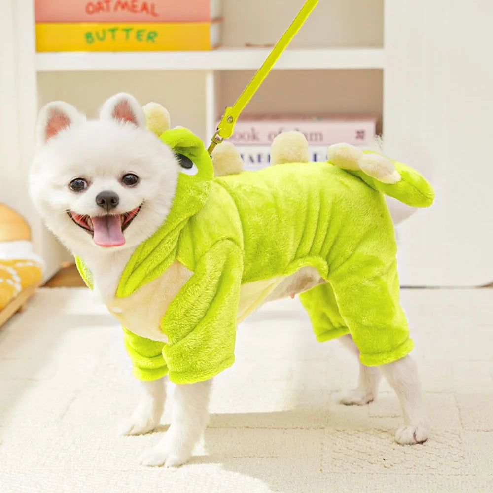 Small white dog wearing a green dinosaur costume on a leash indoors.