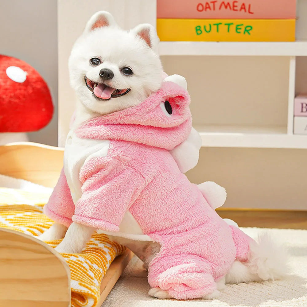 Small white dog wearing a pink outfit sitting on a bed.