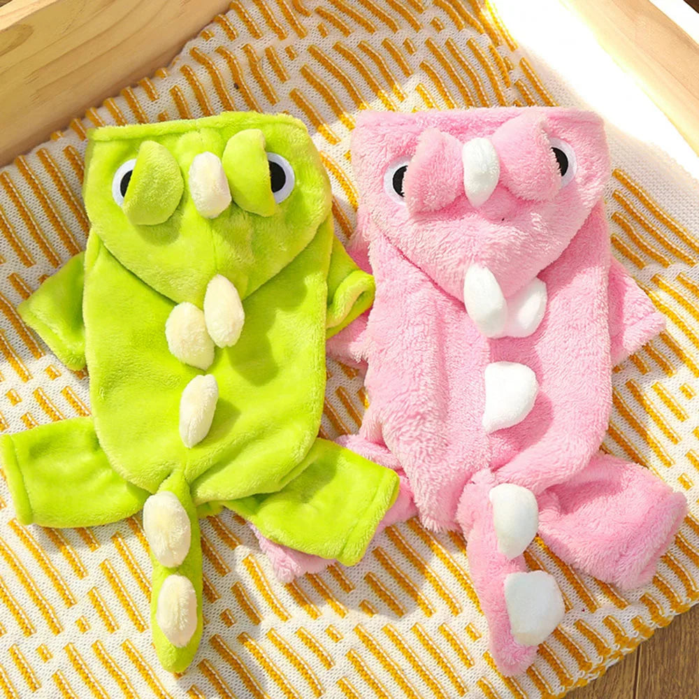 Two plush dog outfits , one green and one pink, on a textured surface.