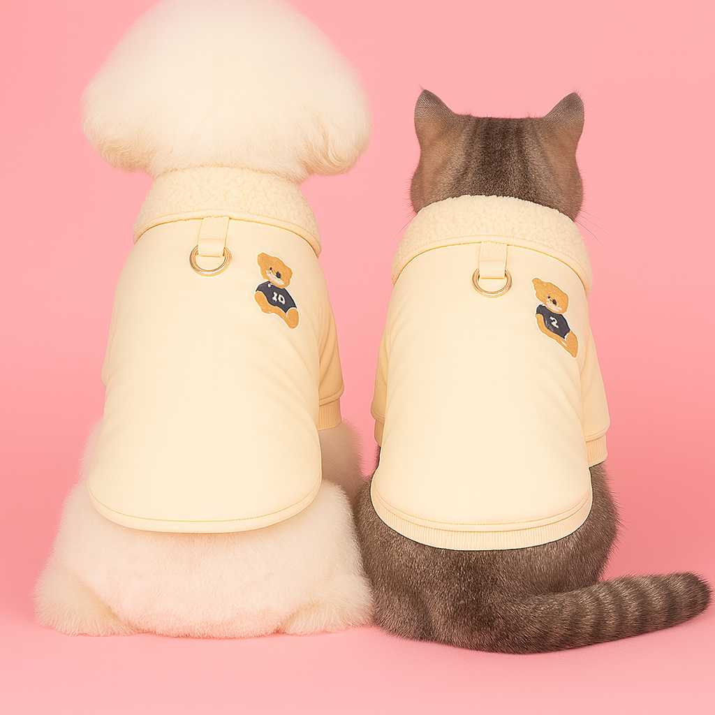 Two small animals, likely a dog and a cat, wearing matching yellow outfits with teddy bear designs on a pink background.